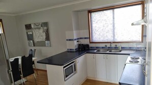 A compact kitchen with a microwave, sink, and stove. There is a dining area with chairs and a table. A window provides natural light. - *WI-FI & Netflix* Super Comfy Accom, 21meter Long  Boat Parking Available!! (Portland)