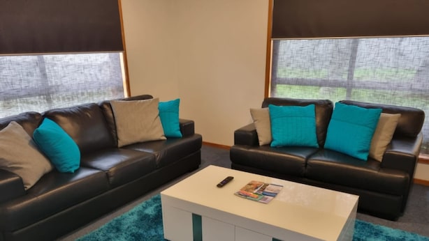 A living room with two black leather sofas, each with teal and beige cushions, a white coffee table with magazines, and a teal rug. - *WI-FI & Netflix* Super Comfy Accom, 21meter Long  Boat Parking Available!! (Portland)