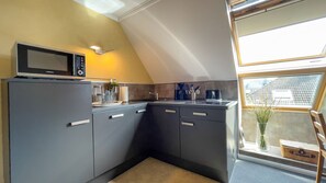 A compact kitchen with a microwave, cabinets, and a window. - Haus Leuchtfeuer - Haus Leuchtfeuer - Bright vacation rental near the beach with (Cuxhaven)