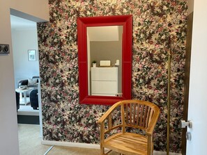 A room with a floral wallpaper, a red-framed mirror, a wooden chair, and a white cabinet. - Haus Leuchtfeuer - Haus Leuchtfeuer - Bright vacation rental near the beach with (Cuxhaven)