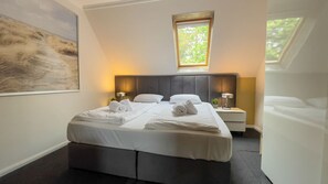 A neatly made double bed with white linens and towels, a bedside table with a lamp, and a large window with a view of greenery. - Leuchtfeuer Voßhörn - House Leuchtfeuer - Bright, beachfront vacation apartment with (Cuxhaven)