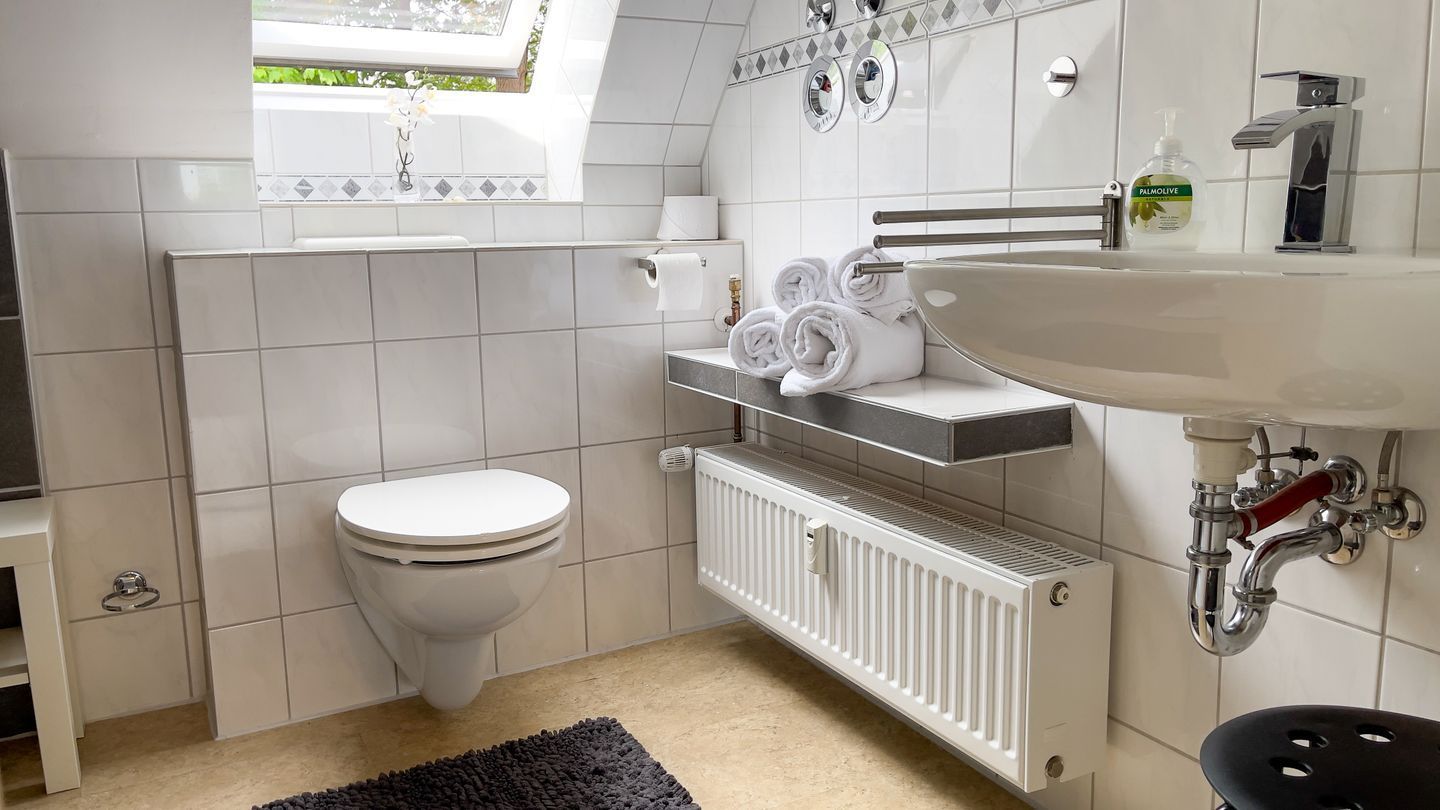 A modern bathroom with a white toilet, a built-in sink, and a radiator below the mirror.