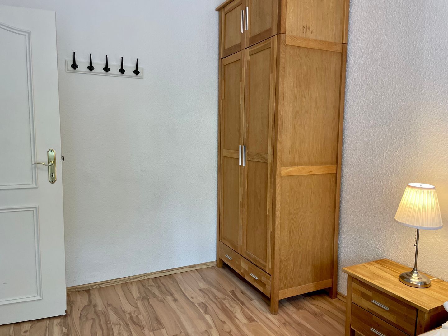 Ein Zimmer mit einem Holzschrank, einem Nachttisch mit Lampe und einer Tür mit Schloss.