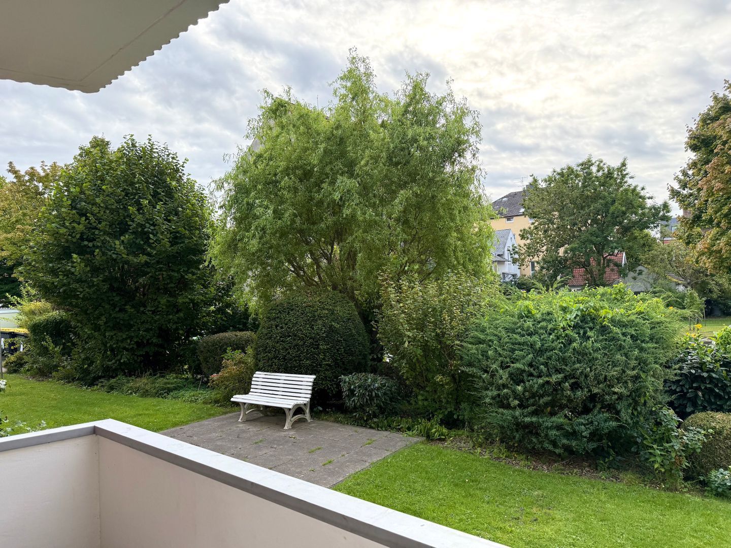 Een tuin met een bankje, weelderige begroeiing en een heldere lucht.