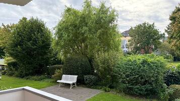 Een tuin met een bankje, weelderige begroeiing en een heldere lucht.