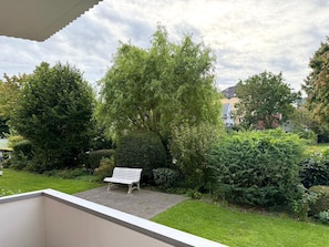 Un jardín con un banco, abundante vegetación y un cielo despejado.