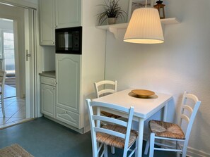 A compact kitchen with white cabinetry, a microwave, and a dining table with two chairs.