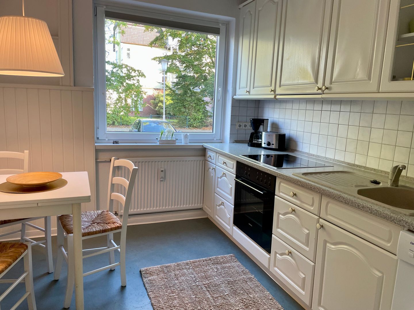 Eine Küche mit weißen Schränken, einem Fenster, einem Esstisch mit Stühlen und einer Kaffeemaschine.