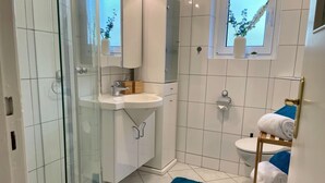 Un bagno moderno con cabina doccia in vetro, lavandino bianco e tappetino da bagno blu.