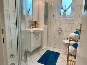 A modern bathroom with a glass shower enclosure, a white sink, and a blue bath mat. - Haus Jenina - House Jenina - Directly on the dike, modern vacation apartment for up to 6 persons (Cuxhaven)