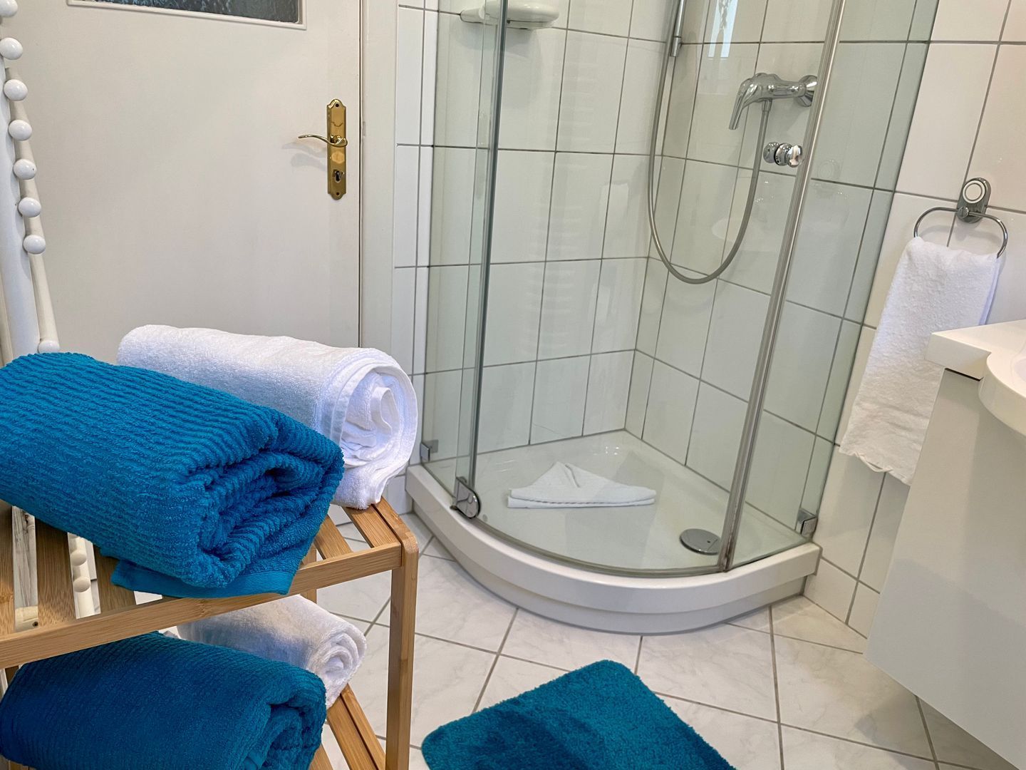 Een badkamer met een douche met glazen wand, witte tegels en een houten plank met opgevouwen handdoeken.