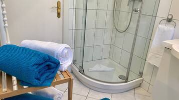Een badkamer met een douche met glazen wand, witte tegels en een houten plank met opgevouwen handdoeken.