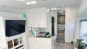 Una cocina compacta con armarios blancos, televisor integrado y un lavamanos.