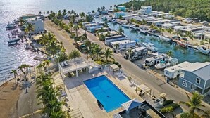 Vista aérea de una zona costera con un puerto deportivo, vehículos recreativos y una piscina.