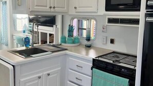 Una cocina compacta con armarios blancos, microondas integrado, estufa y lavabo.