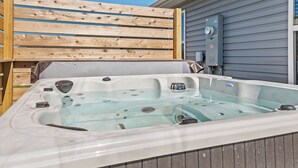 Ein Whirlpool mit einer Holzterrasse und ein graues Haus im Hintergrund.