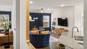Ein modernes Wohnzimmer mit einem dunkelblauen Sofa, Deckenventilator, Flachbildfernseher und Küchenbereich mit Granitarbeitsplatte und Spüle.