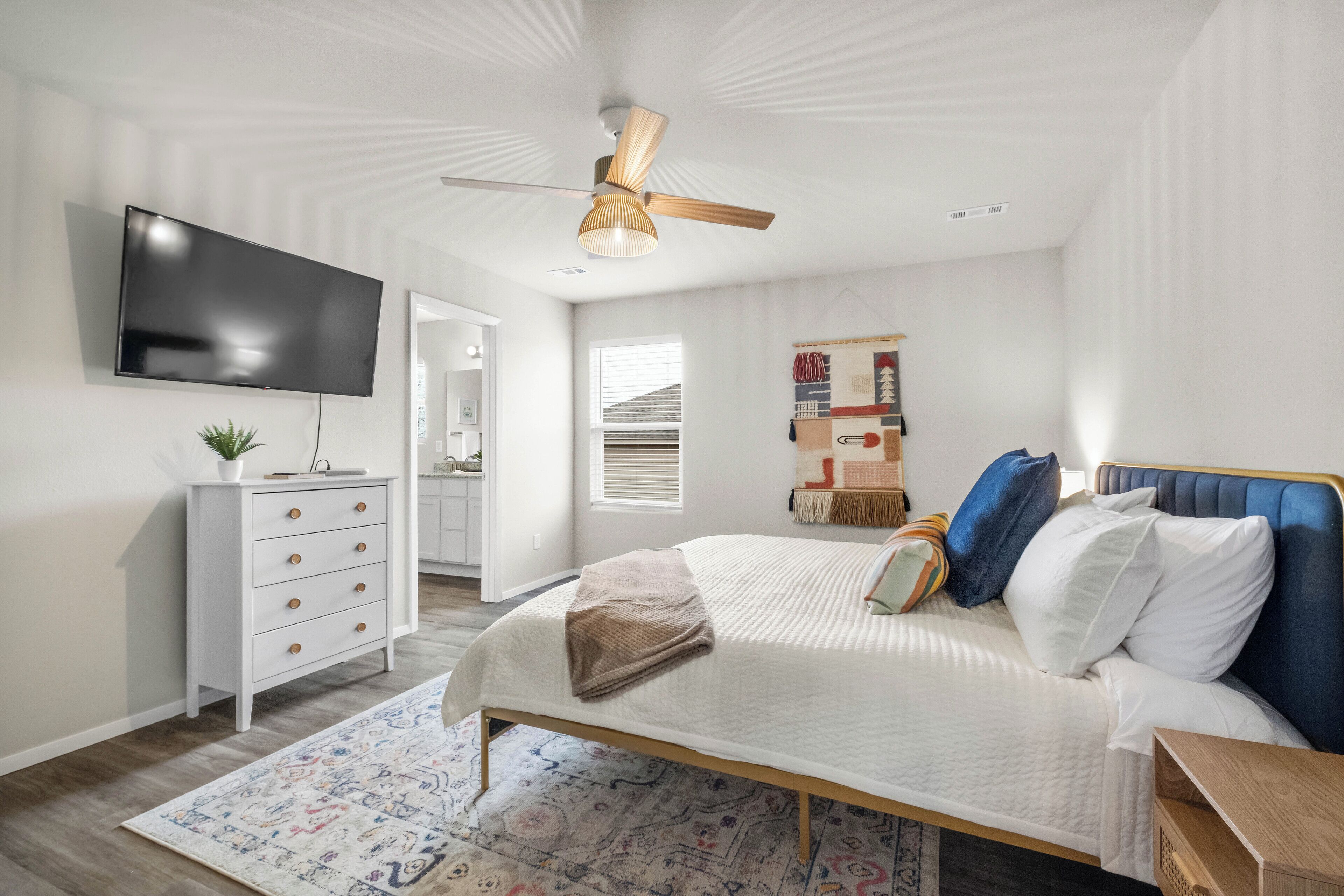 Ein Schlafzimmer mit Bett, Fernseher, Deckenventilator, Kommode und Fenster.