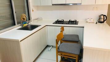 A compact kitchen with a sink, stove, and two wooden chairs.