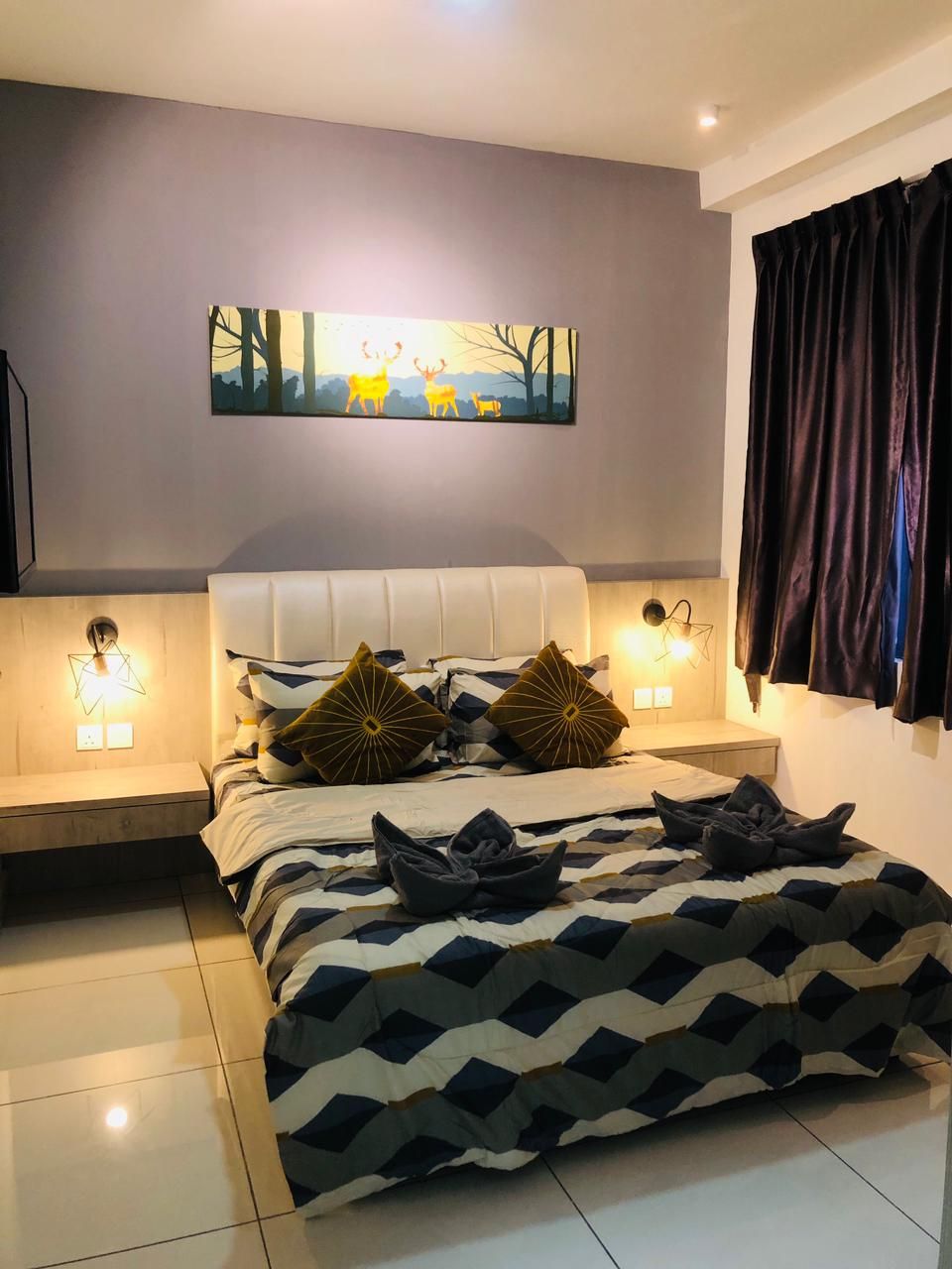 Une chambre à coucher moderne avec un grand lit, une literie à motifs géométriques, deux lampes fixées au mur et un tableau représentant des cerfs accroché au mur.