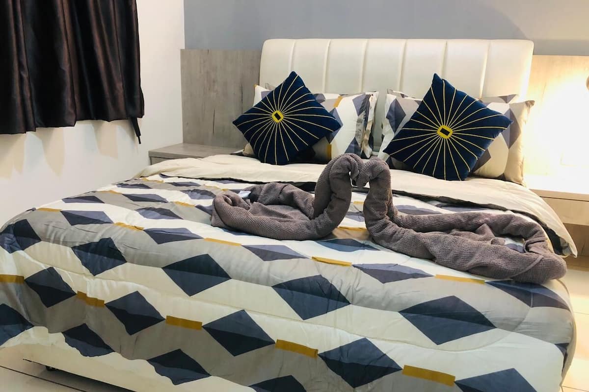 Uma cama com colcha de padrão geométrico, duas almofadas decorativas e cabeceira.