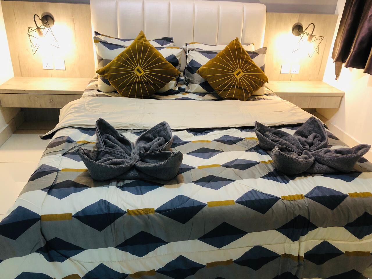 A neatly made bed with a geometric patterned duvet, two decorative pillows, and folded towels on the bed.