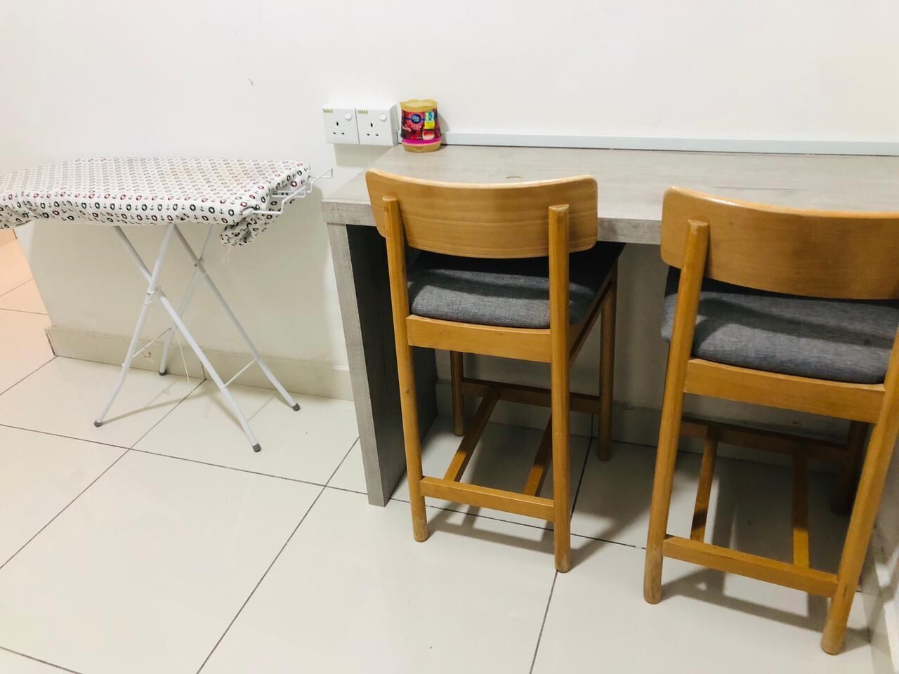 A small kitchenette with two wooden chairs, a table with a patterned tablecloth, and a can of food on the counter.