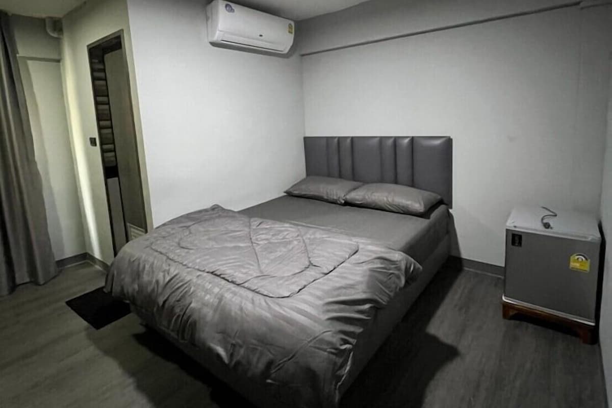 Ein Zimmer mit einem Bett, einer Klimaanlage, einem kleinen Tisch und einer Tür.