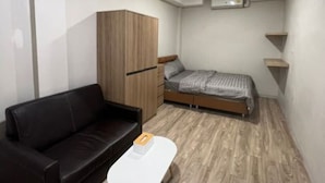 A compact room with a bed, a black leather sofa, a small white table, and a wooden wardrobe. - W71  (Bangkok)