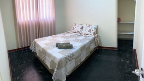 Un dormitorio con cama, ventana con cortinas, armario y puerta.