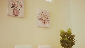 Una habitación con una mesa redonda, dos sillas, una planta en maceta y dos cuadros colgados en la pared.