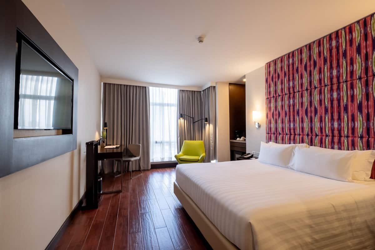 A hotel room with a large bed, a desk with a chair, a television, and a window with curtains.