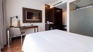 Habitación de hotel con una cama grande, un escritorio con silla, un televisor montado en la pared y una pequeña zona de kitchenette.