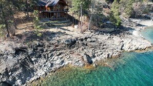 Eine Holzblockhütte mit Balkon, umgeben von Bäumen und einer felsigen Küstenlinie.