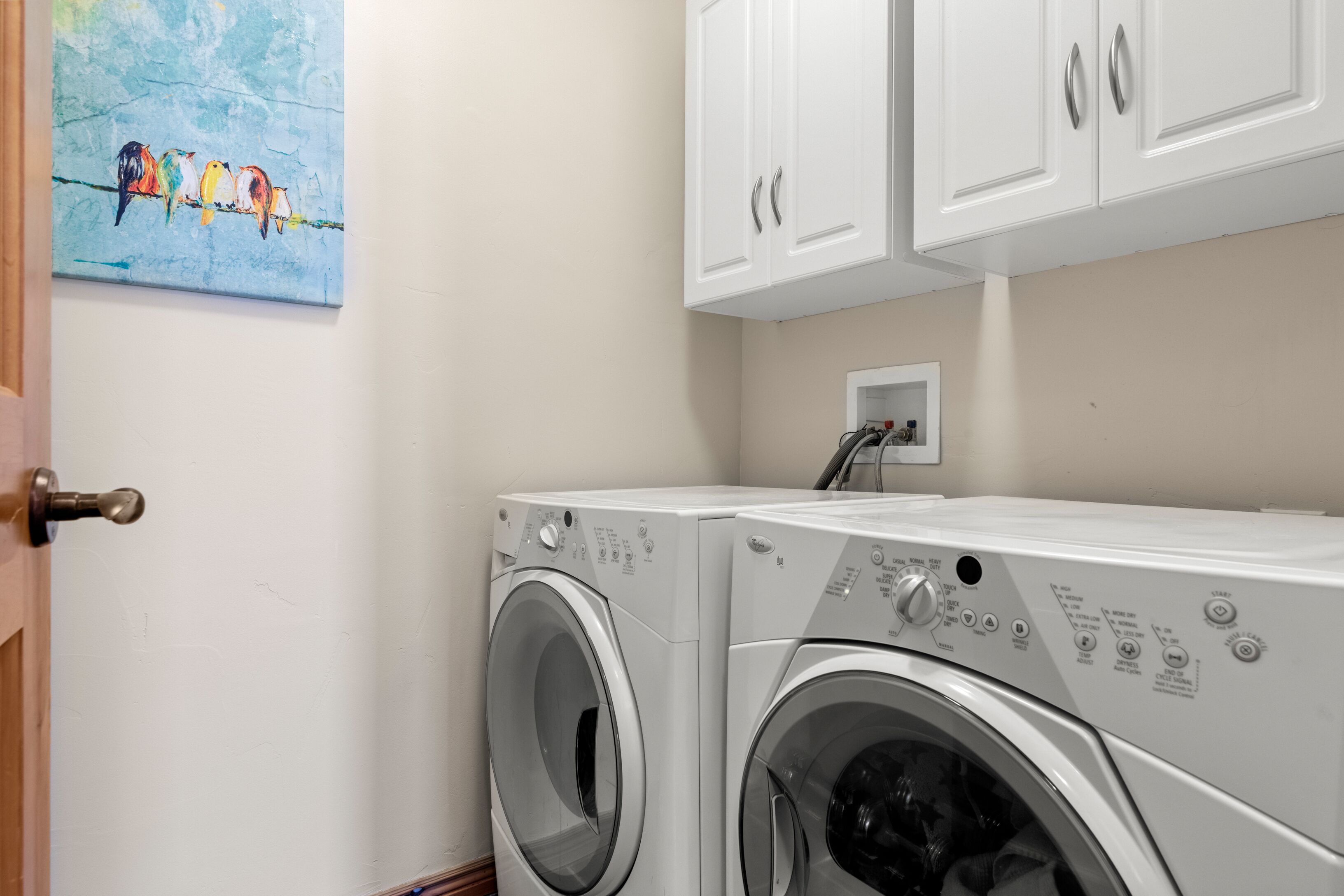 A laundry area with two front-loading washing machines, a wall-mounted electrical outlet, and a door with a brass doorknob.