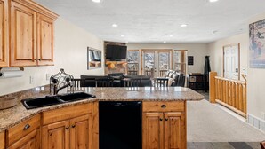 Una cocina con armarios de madera, encimera de granito y lavavajillas. Cuenta con una zona de comedor con mesa y sillas.