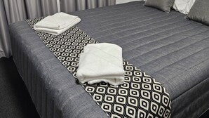 A neatly made bed with a patterned bedspread, pillows, and folded towels. - Leeton Centre Motel (Leeton)