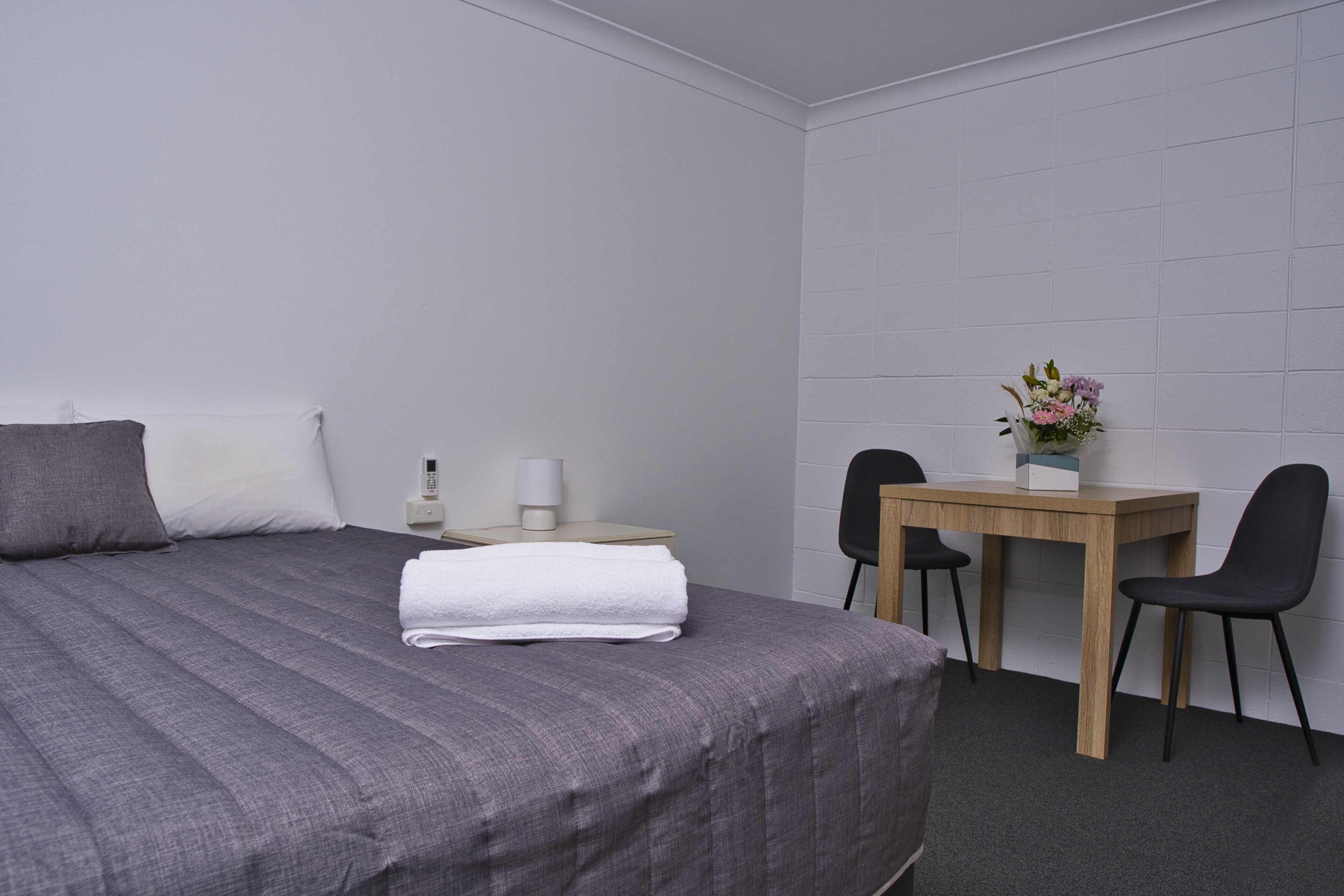 A hotel room with a bed, a desk, two chairs, a small table with a vase of flowers, and a telephone on the nightstand.