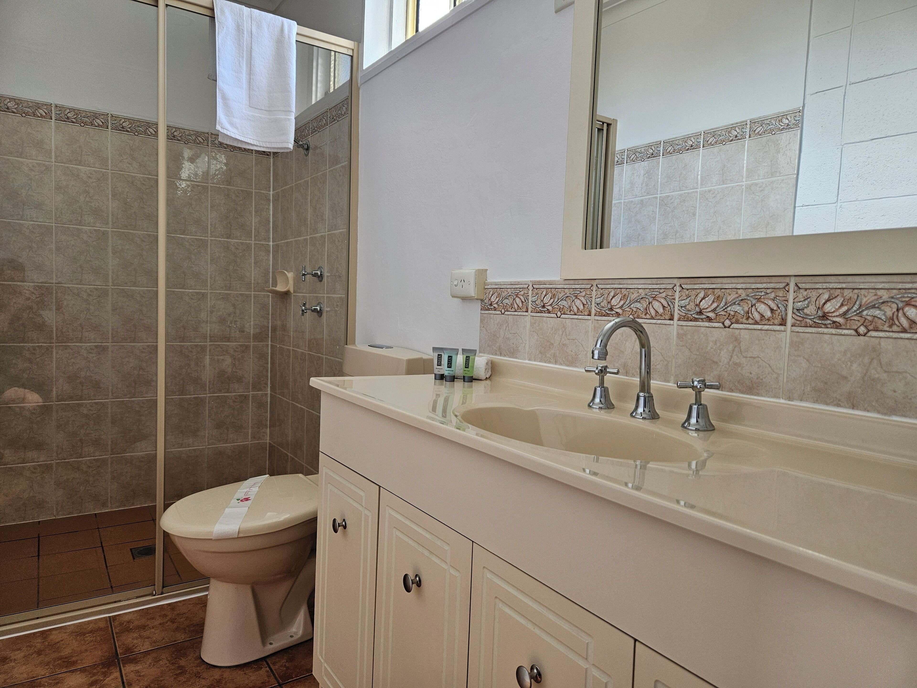 A bathroom with a shower, toilet, sink, and cabinets.