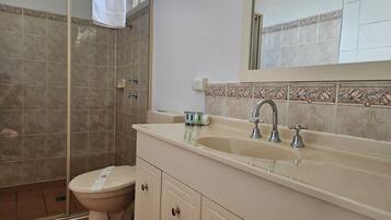 A bathroom with a shower, toilet, sink, and cabinets.