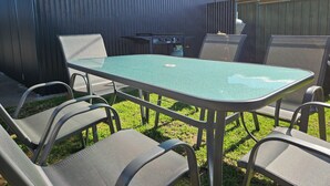 An outdoor patio with a rectangular table and six chairs, surrounded by a metal fence and a wooden structure. - Leeton Centre Motel (Leeton)