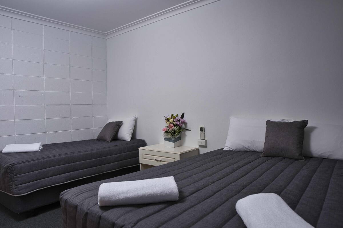 A hotel room with two beds, a bedside table with a vase of flowers, and a white wall with a grid pattern.