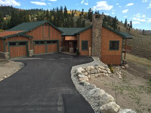 A two-story log cabin with a stone chimney, a garage, and a driveway leading to the entrance. - Amazing View Mountain Home - Private Neighborhood (Silverthorne)