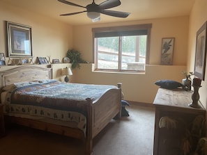 A bedroom with a wooden bed, a ceiling fan, a window with a view, and framed pictures on the wall. - Amazing View Mountain Home - Private Neighborhood (Silverthorne)