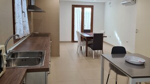 Une cuisine moderne dotée d’un évier encastré, d’un coin repas avec une table et des chaises, et d’une grande fenêtre agrémentée de rideaux.