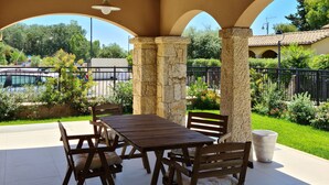 Une terrasse ext érieure avec une table et des chaises en bois, des piliers en pierre et une vue sur un jardin et une piscine.