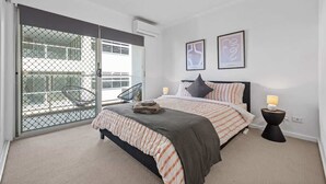 A bedroom with a bed, a nightstand, a chair, and a balcony with a mesh door. - Hipster Loft! ~  1Bed/Study/1Bath/Balconies/1Car (Fortitude Valley)