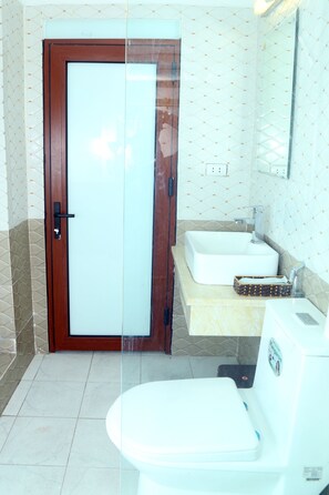 A bathroom with a wooden door, a white sink, and a toilet. - Luxury Airport Hotel & Travel (Hanoi)