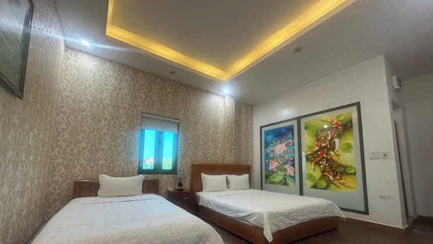 A hotel room with two beds, a window with blinds, a ceiling light, and two wall-mounted air conditioning units. - Luxury Airport Hotel & Travel (Hanoi)