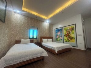Habitación de hotel con dos camas, una ventana con persianas, una lámpara en el techo y dos unidades de aire acondicionado fijadas a la pared.